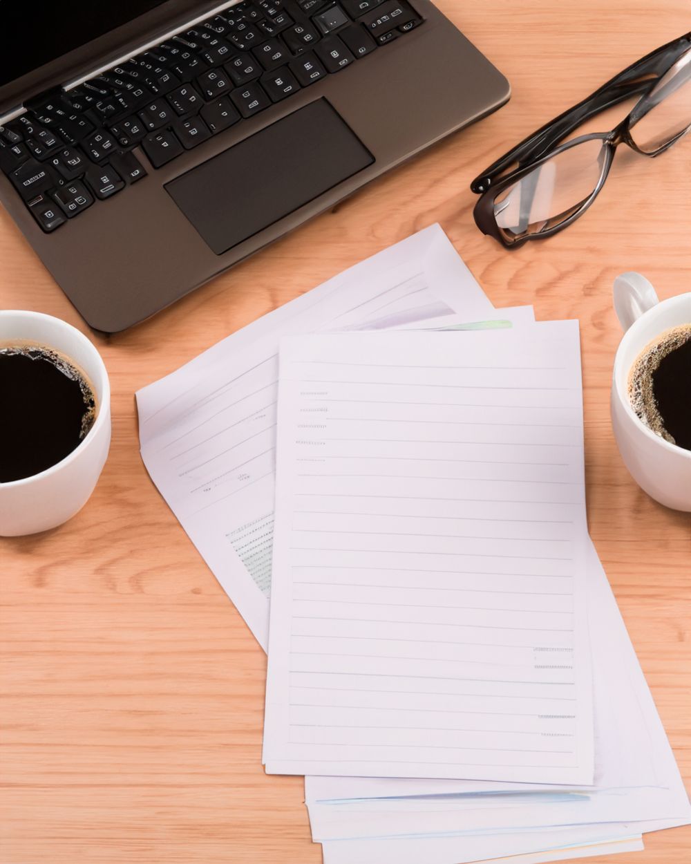 Paperwork, glasses, and coffee beside a laptop