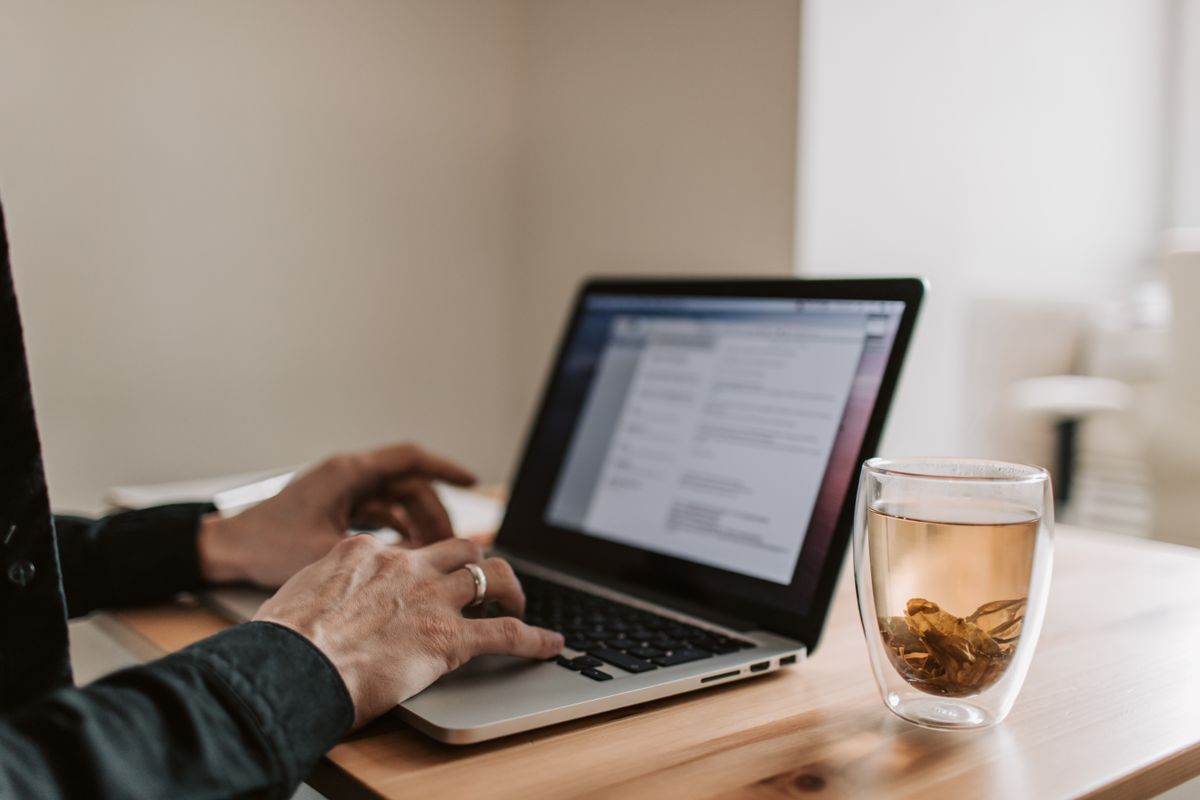 Hands using a laptop beside a cup of tea